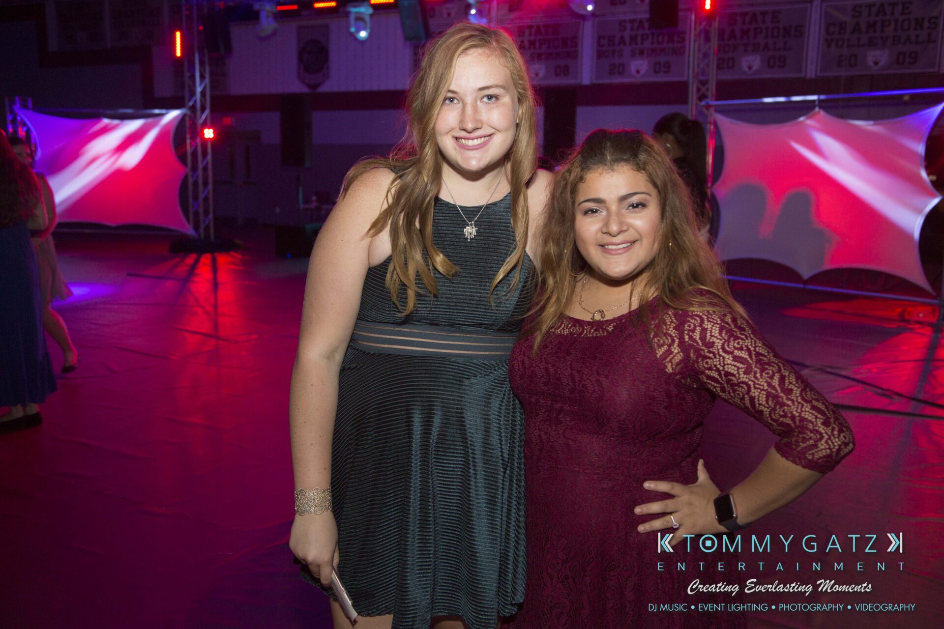 Two people smiling at a party, standing on a dance floor with colorful lighting in the background.
