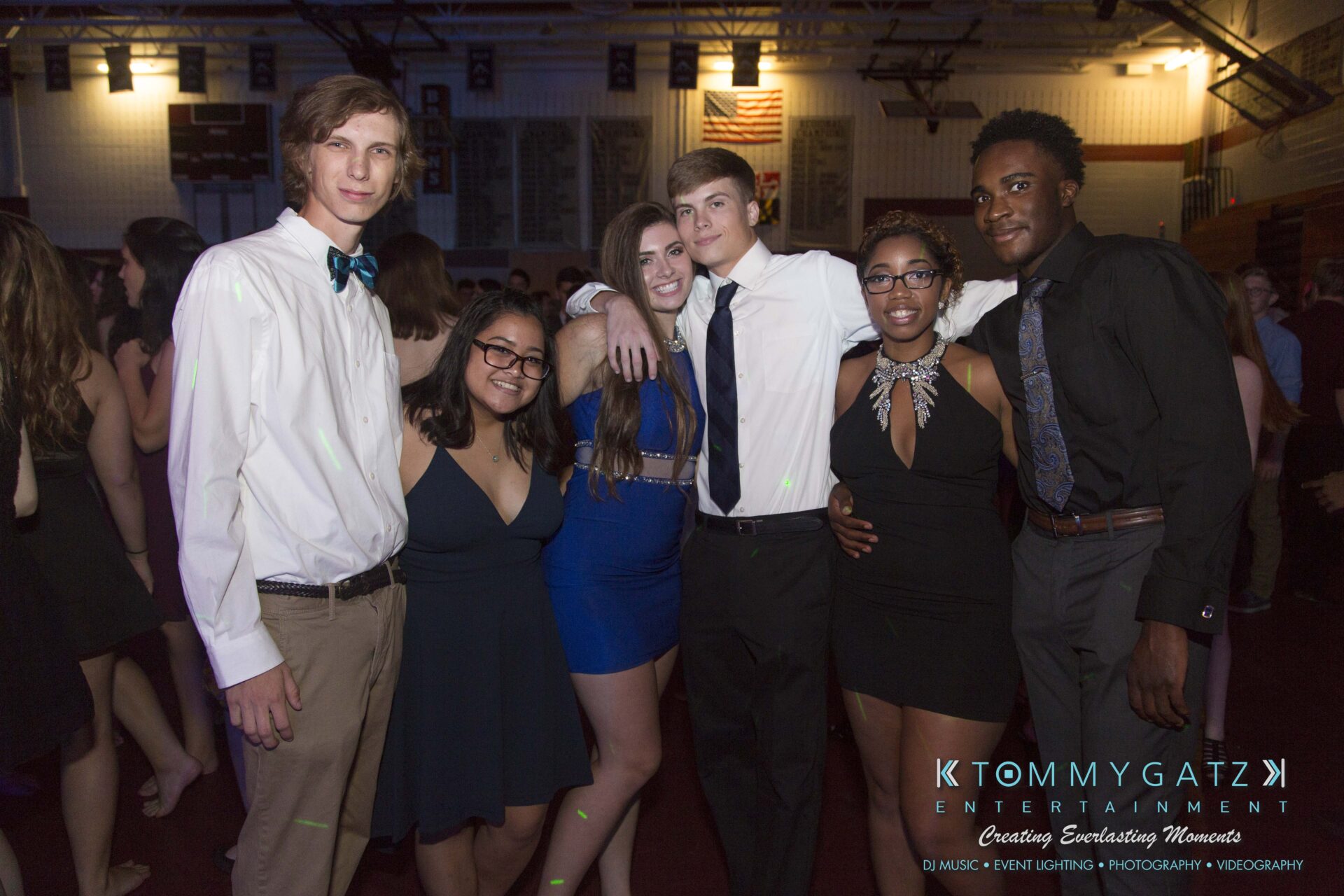 A group of six people dressed in formal attire pose together at an indoor event.