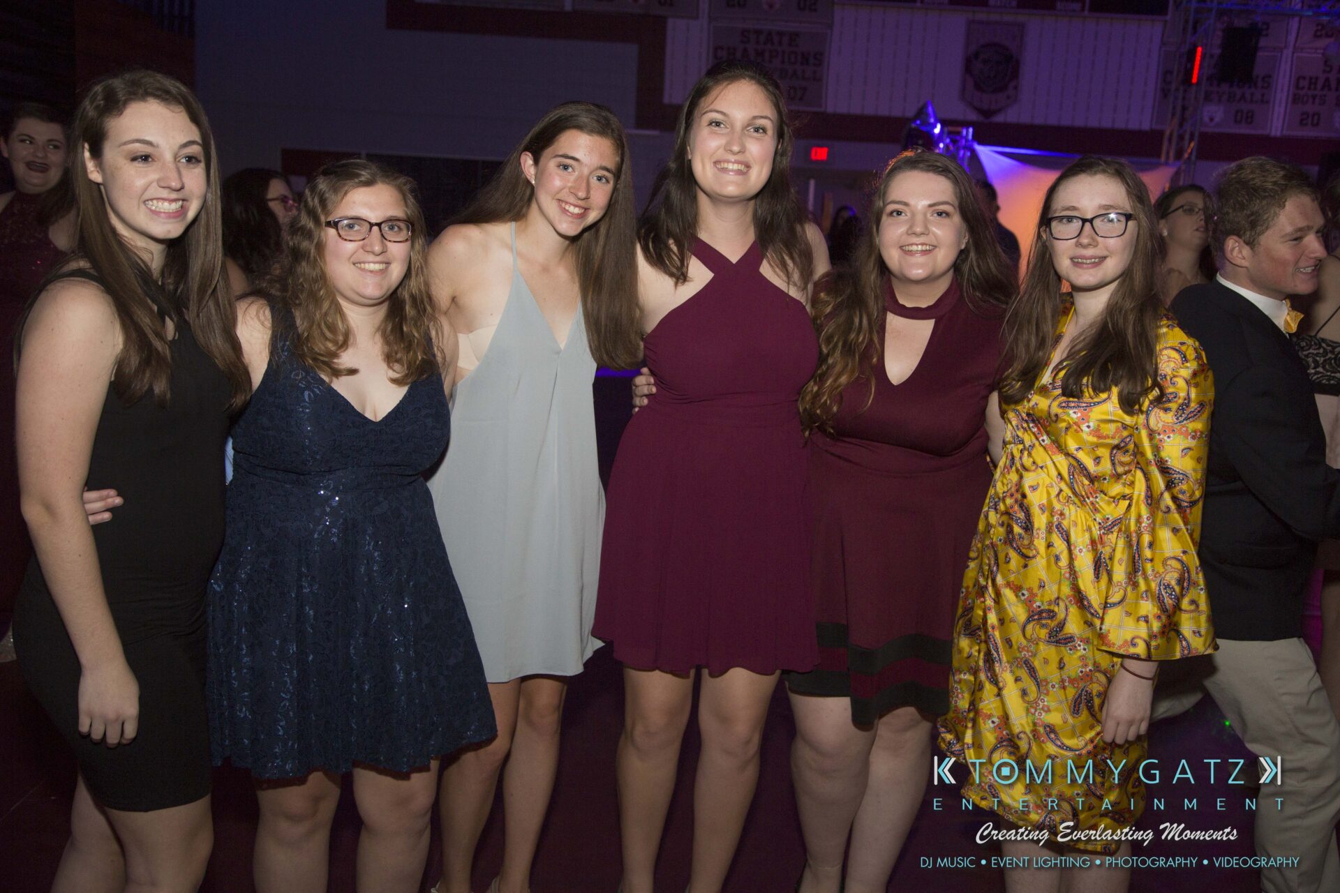 Six people smiling at an indoor event, wearing semi-formal attire.