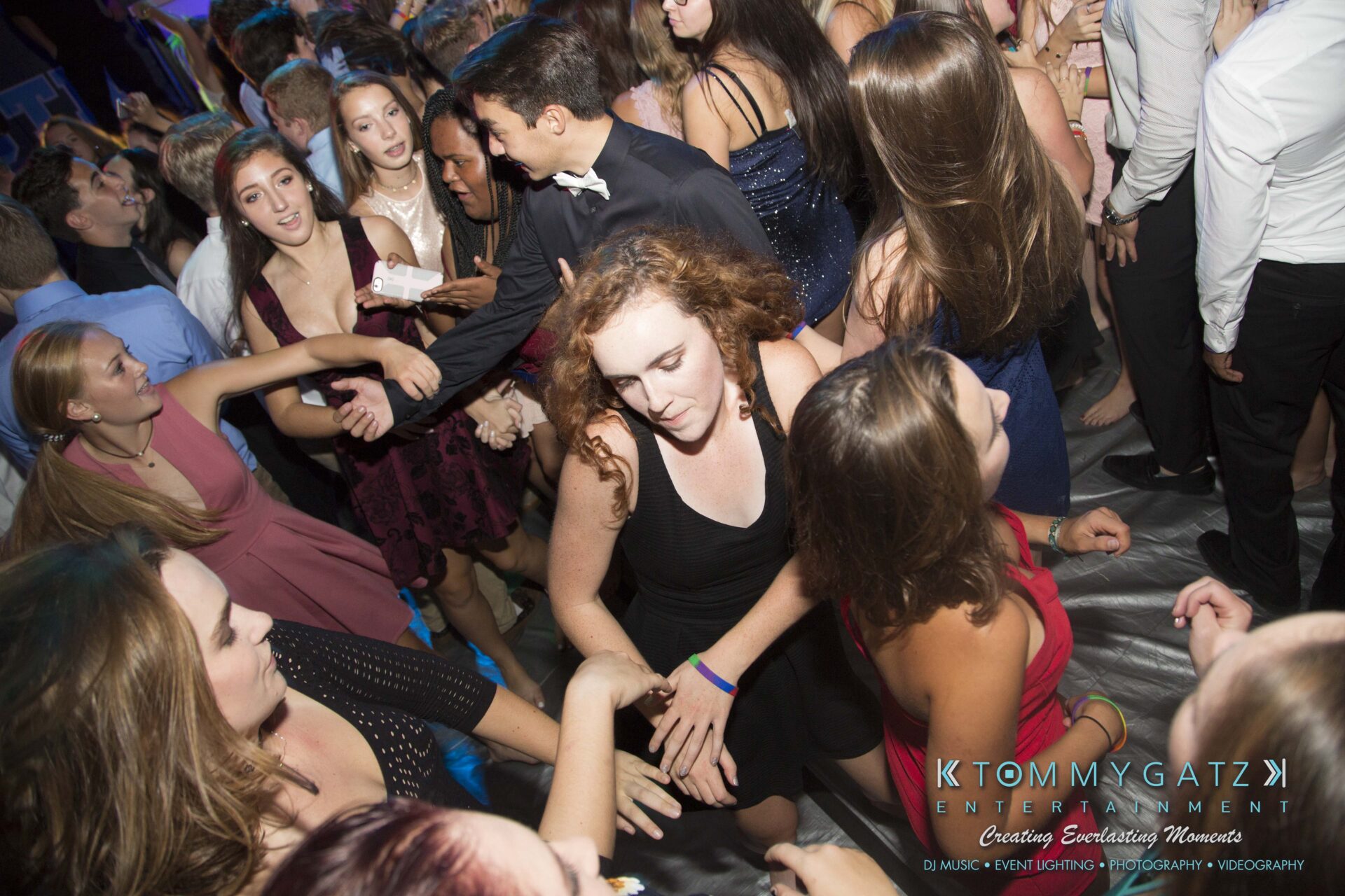 A lively crowd of people, mostly in formal attire, are dancing closely in a dimly lit room.