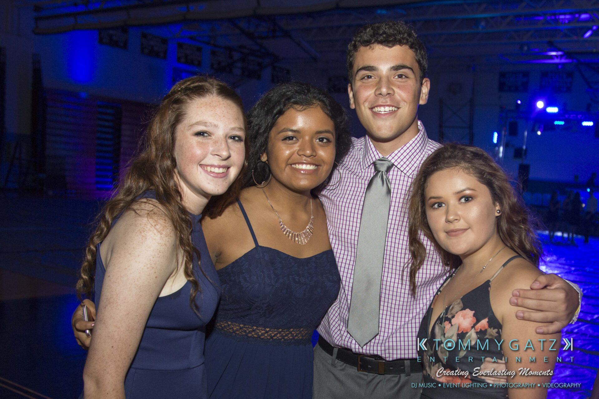 Four people smiling and posing together at an indoor event with blue lighting.
