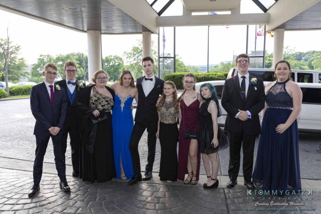 A group of nine young people in formal attire stand together outside a building, posing for a photo.