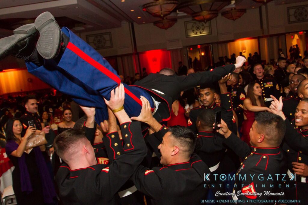 Group of people in formal military uniforms lift a person in the air at a lively indoor event.