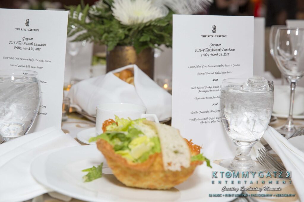 A table setting featuring a plated salad, two glasses of water, and event menus for the 2016 awards luncheon at The Ritz-Carlton.