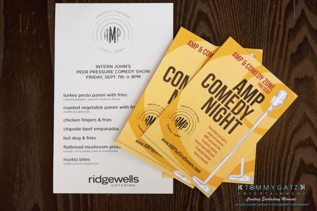 Menu and flyers for AMP Comedy Night event featuring food options like turkey pesto panini and chipotle beef empanadas, with Ridgewells Catering and event details.