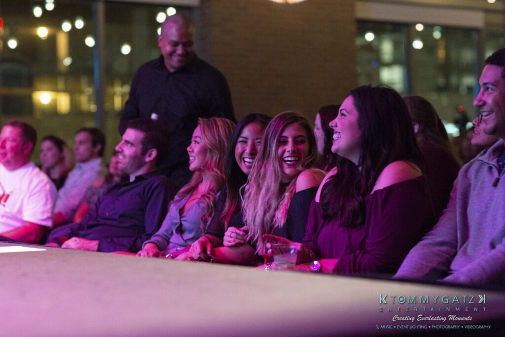 A group of people sitting together, smiling and laughing, at an indoor event.