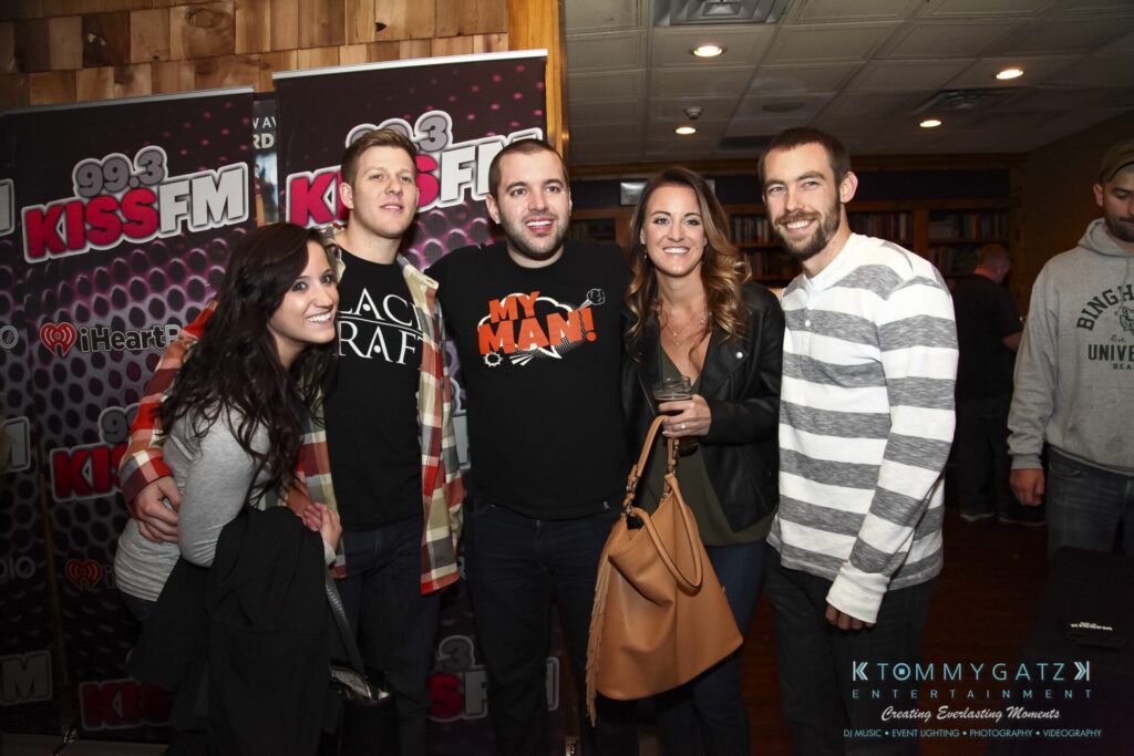 Group of people smiling and posing for a photo in front of a Kiss FM backdrop at an event.