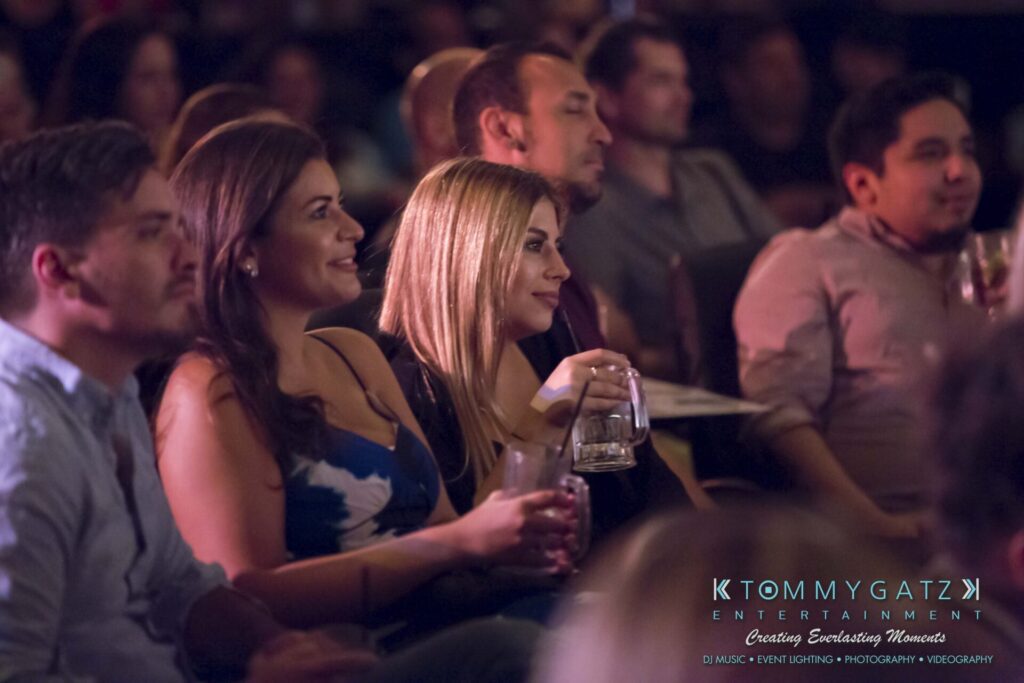 Audience members seated, holding drinks, and watching an event with interest.