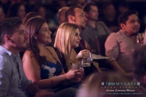 Audience members seated, holding drinks, and watching an event with interest.