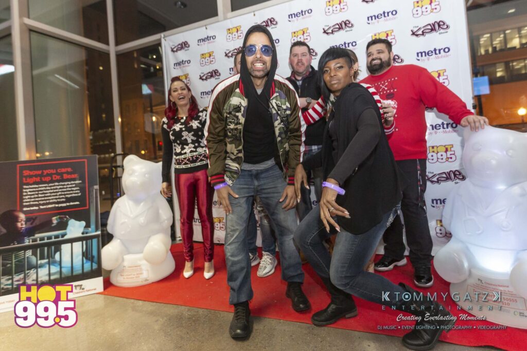 A group of people posing enthusiastically on a red carpet in front of a branded backdrop, with inflatable bear figures on either side.