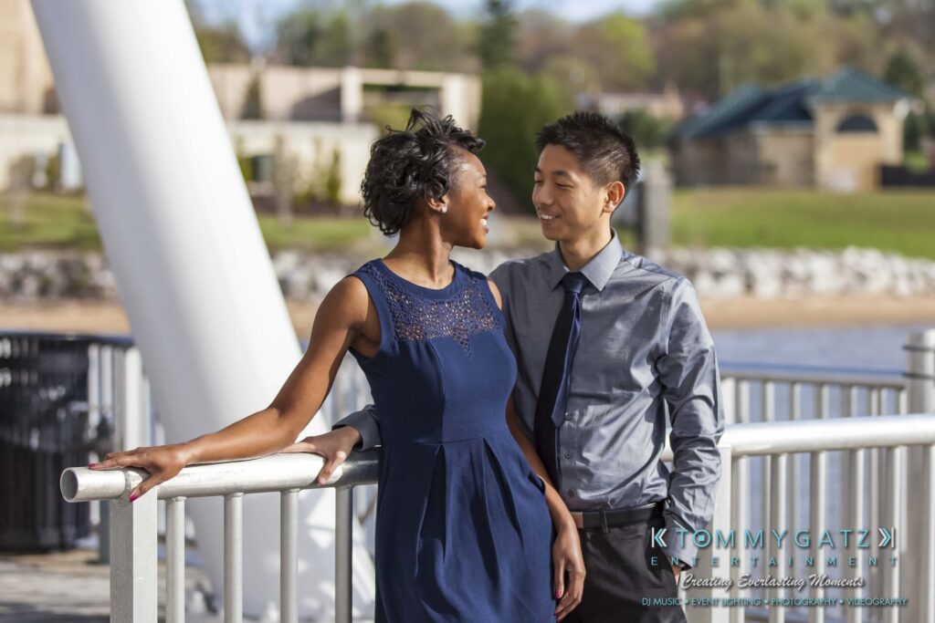 A man and woman smiling at each other while leaning against a railing outdoors.