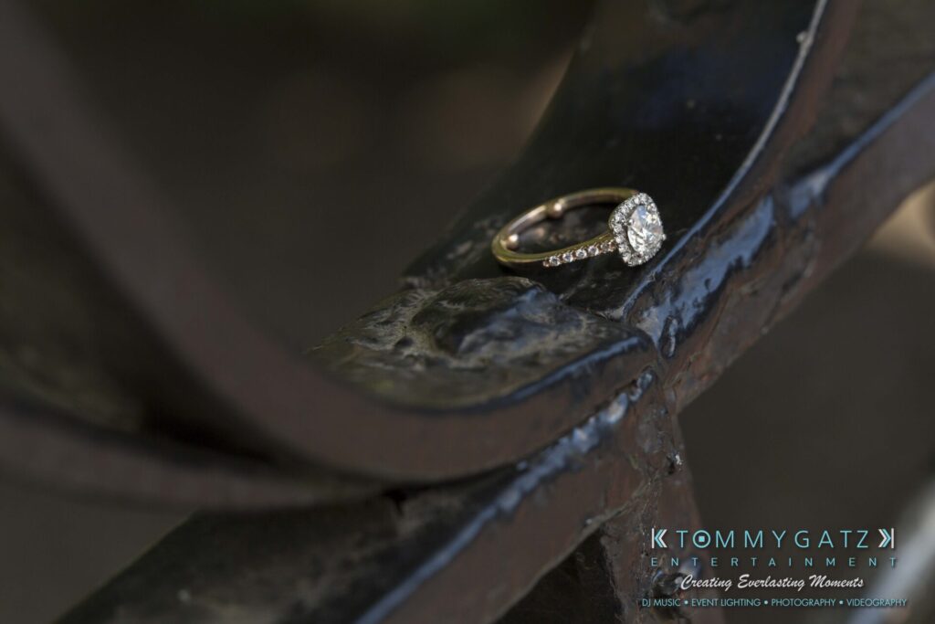 A diamond engagement ring rests on a curved metal surface.