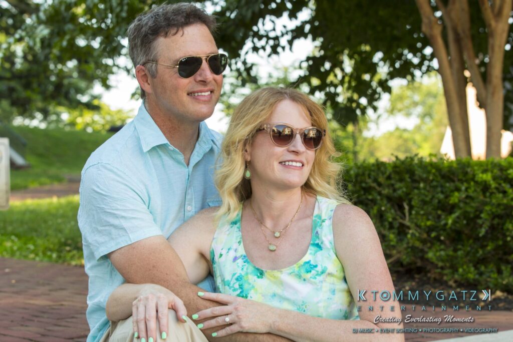 A couple sits together outdoors on a sunny day, both wearing sunglasses.