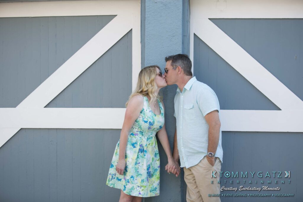 A couple holds hands and kisses in front of a large gray and white wooden door.