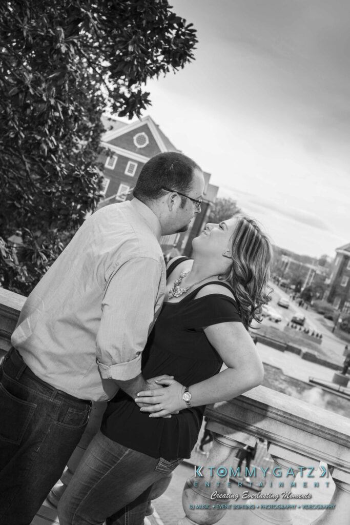 A couple stands on a balcony overlooking a street, embracing and smiling at each other.