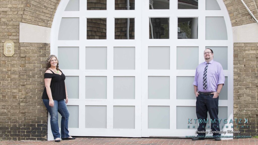 Two people standing in front of a large white door with frosted glass panels, posed on either side, both wearing casual attire.
