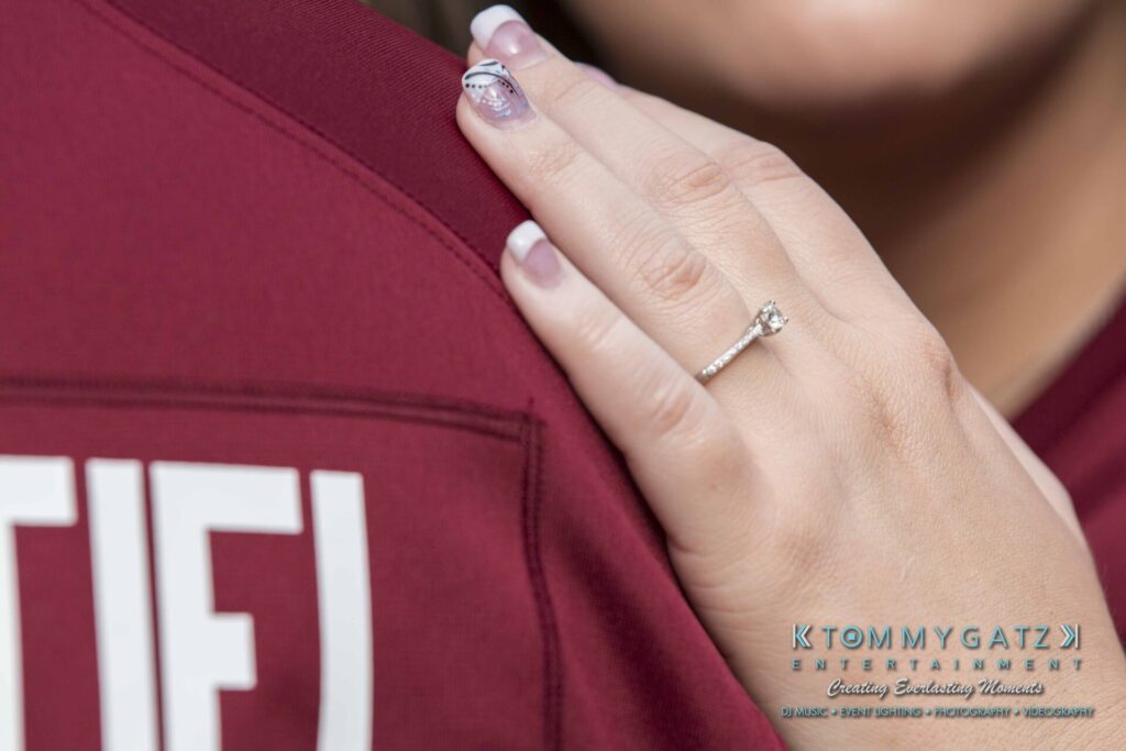 A person with a diamond ring on their finger rests their hand on another person's shoulder, visible in a maroon shirt.