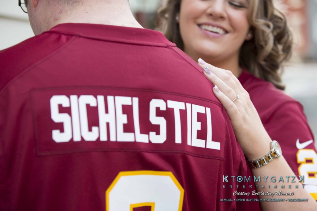 A person in a red sports jersey with the name "Sichelstiel" on the back. Another person smiles and touches their shoulder.