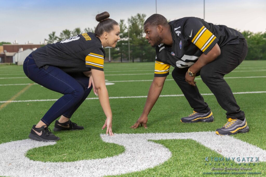 Two people in matching jerseys face each other in a squat position on a football field, near the number 50.