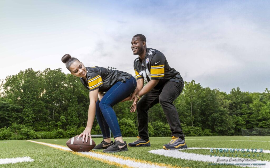 A woman prepares to hike a football while a man stands behind her on a football field. Both are wearing black and yellow sports jerseys.