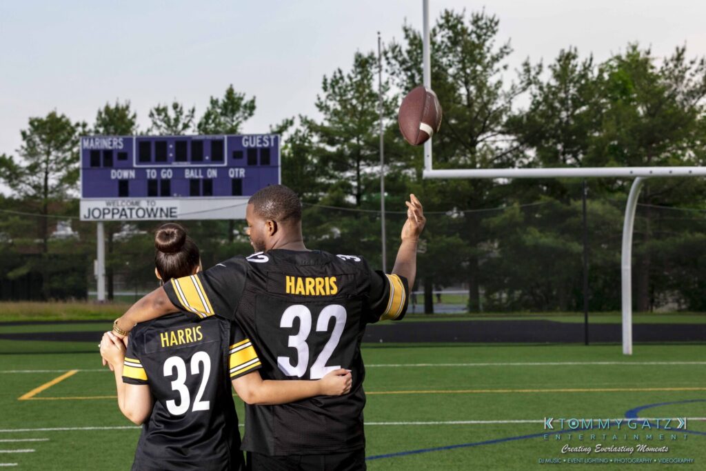Two people in matching jerseys, labeled "Harris 32," stand on a football field. One person is holding a football with an outstretched arm. A scoreboard and goalpost are visible in the background.