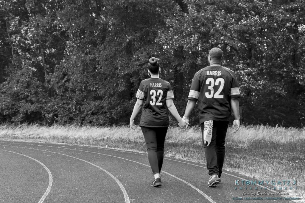 A couple holding hands walks on a track, wearing matching jerseys with the number 32.