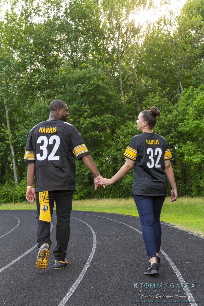 A couple wearing matching jerseys with the number 32 walks hand in hand on a track surrounded by lush greenery.