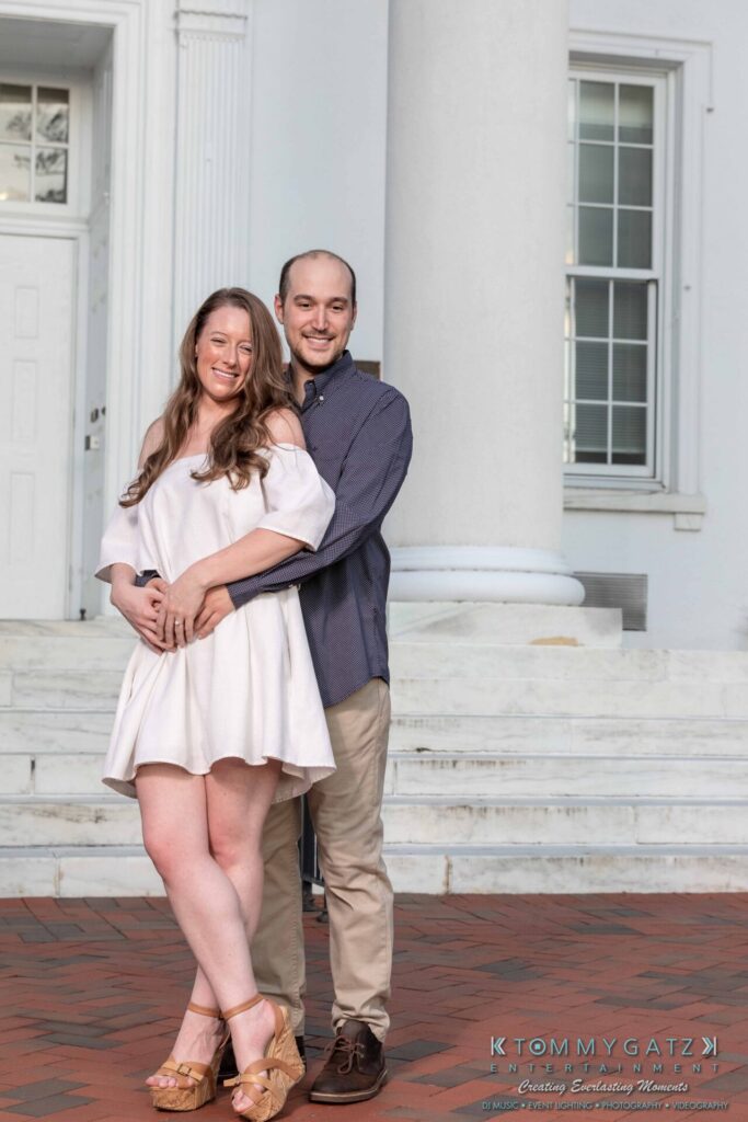 A couple poses on a brick walkway in front of a white building with columns.