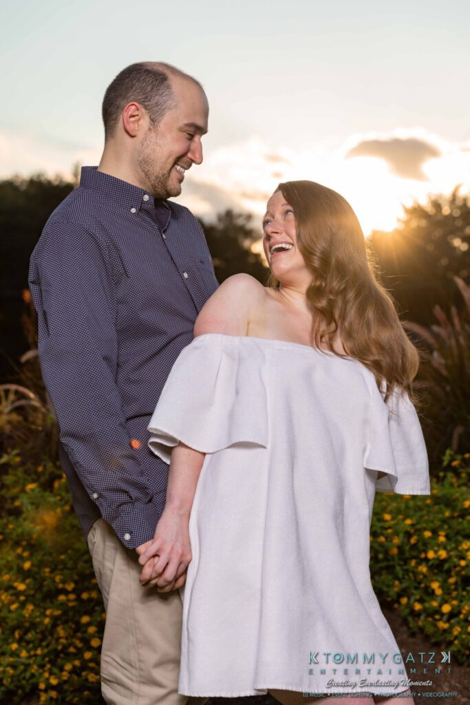 A couple holds hands and smiles at each other in a garden during sunset.