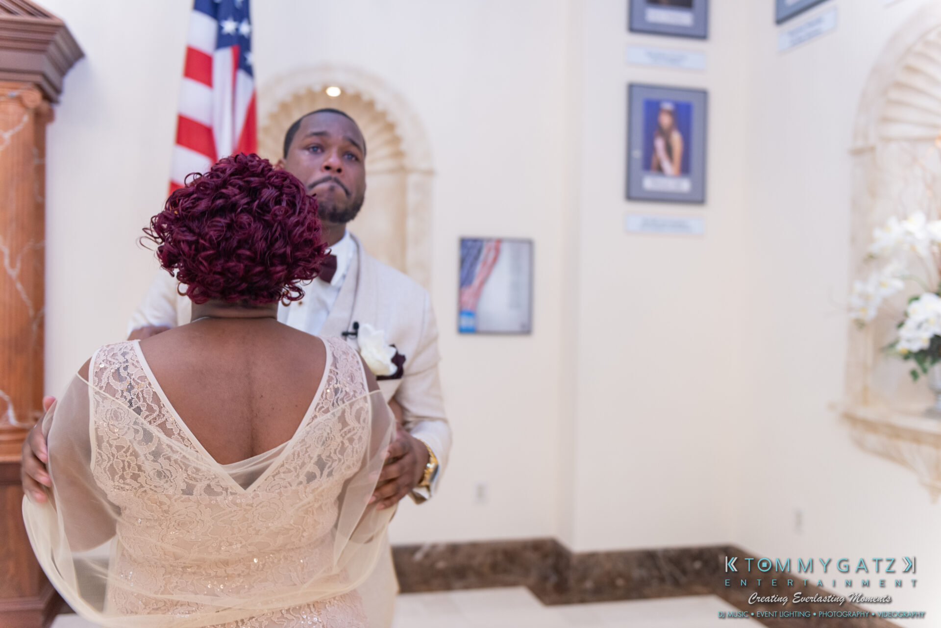 A couple dances together in a formal setting with an American flag and framed pictures on the wall.