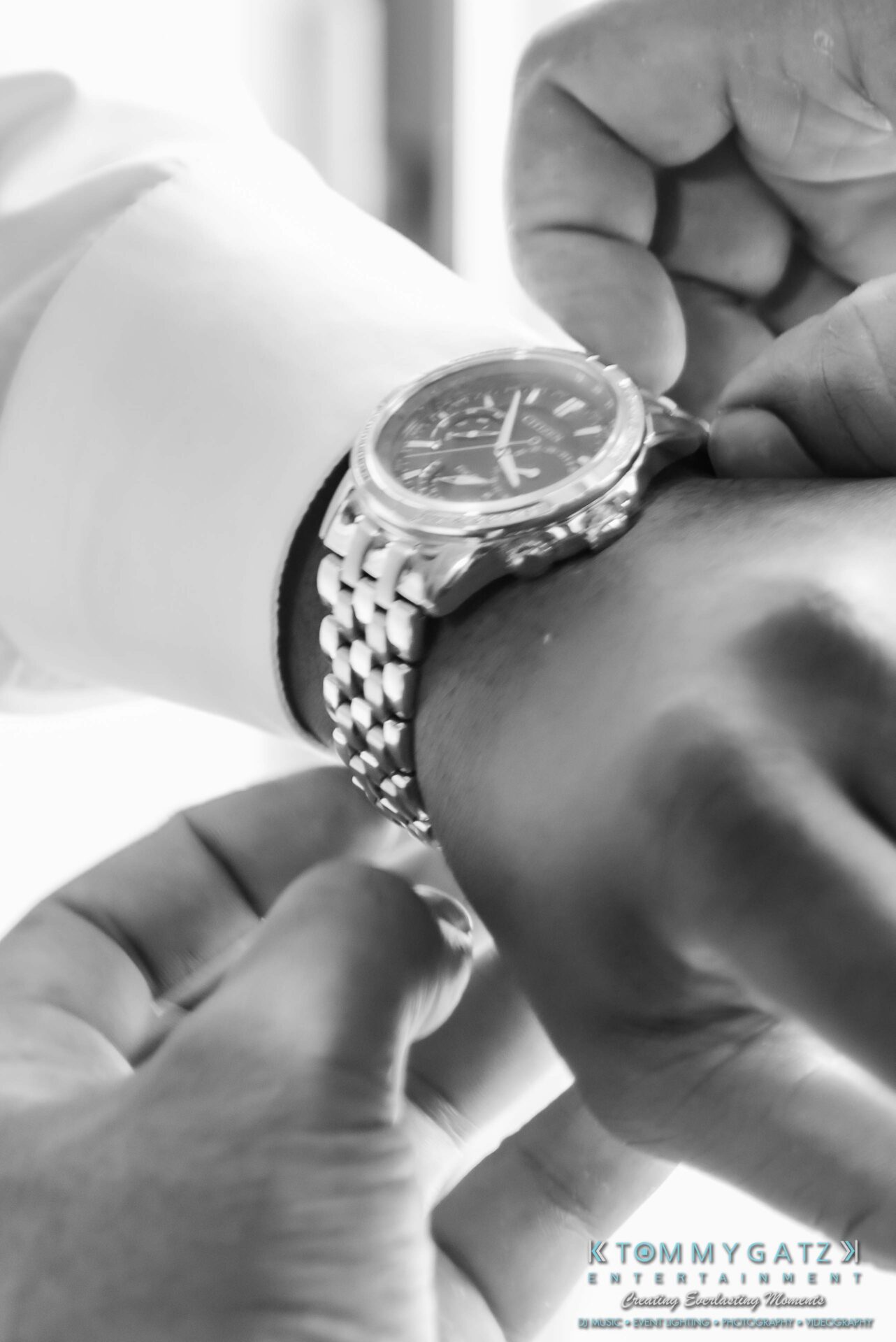 Close-up of a person fastening a silver watch on their wrist. The watch has a circular face and a metal band.