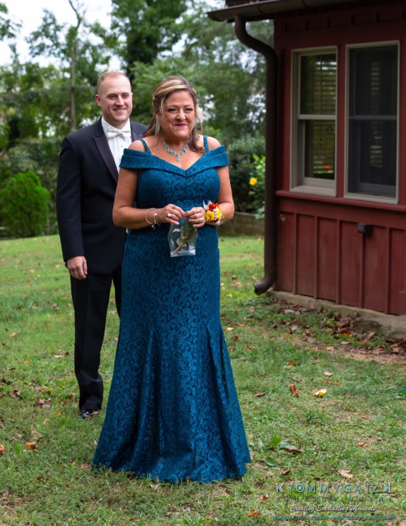 A woman in a blue dress stands in front of a man in a suit outdoors near a building.