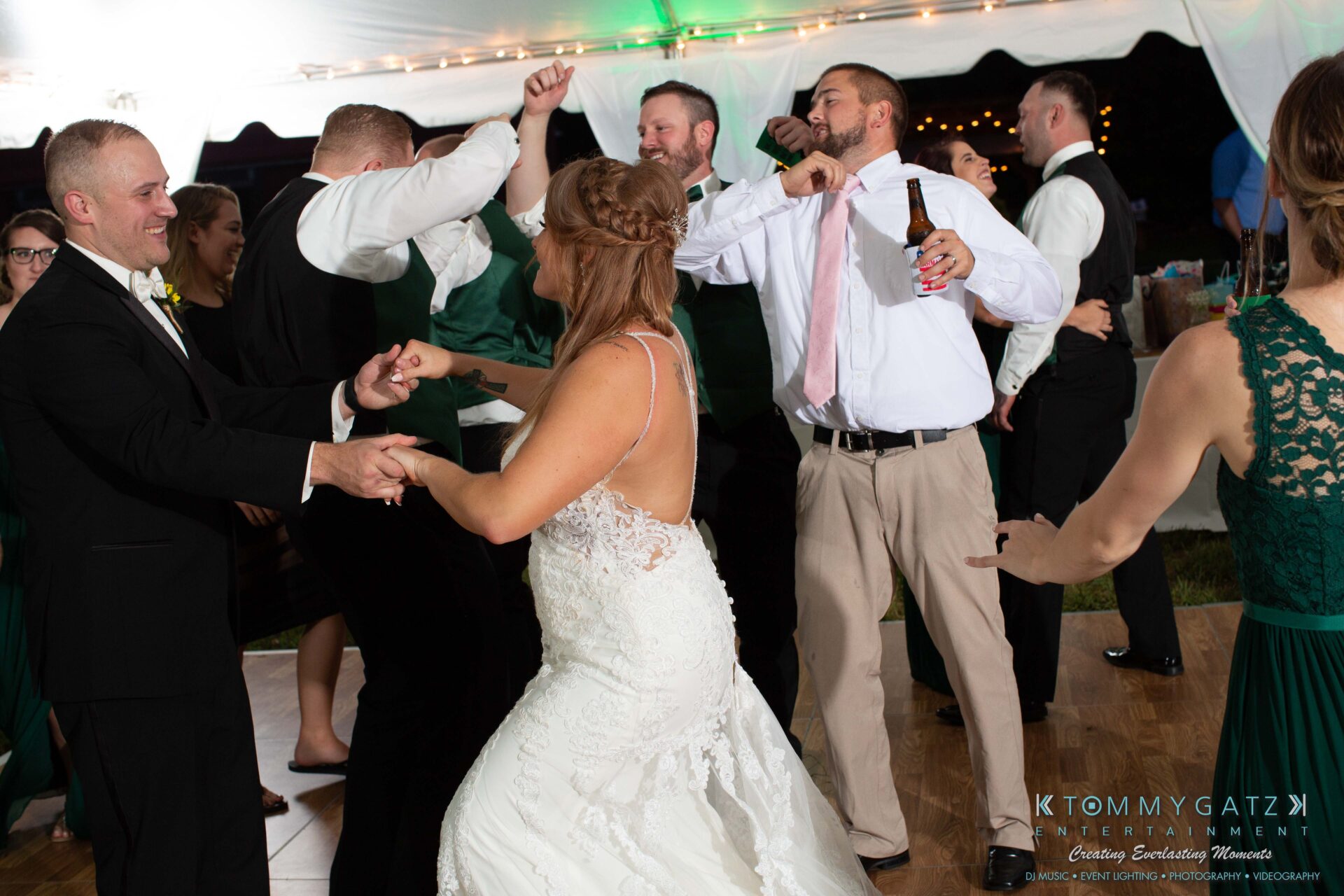 A wedding reception with guests dancing energetically under a tent. A bride in a white gown dances with a guest in formal attire.