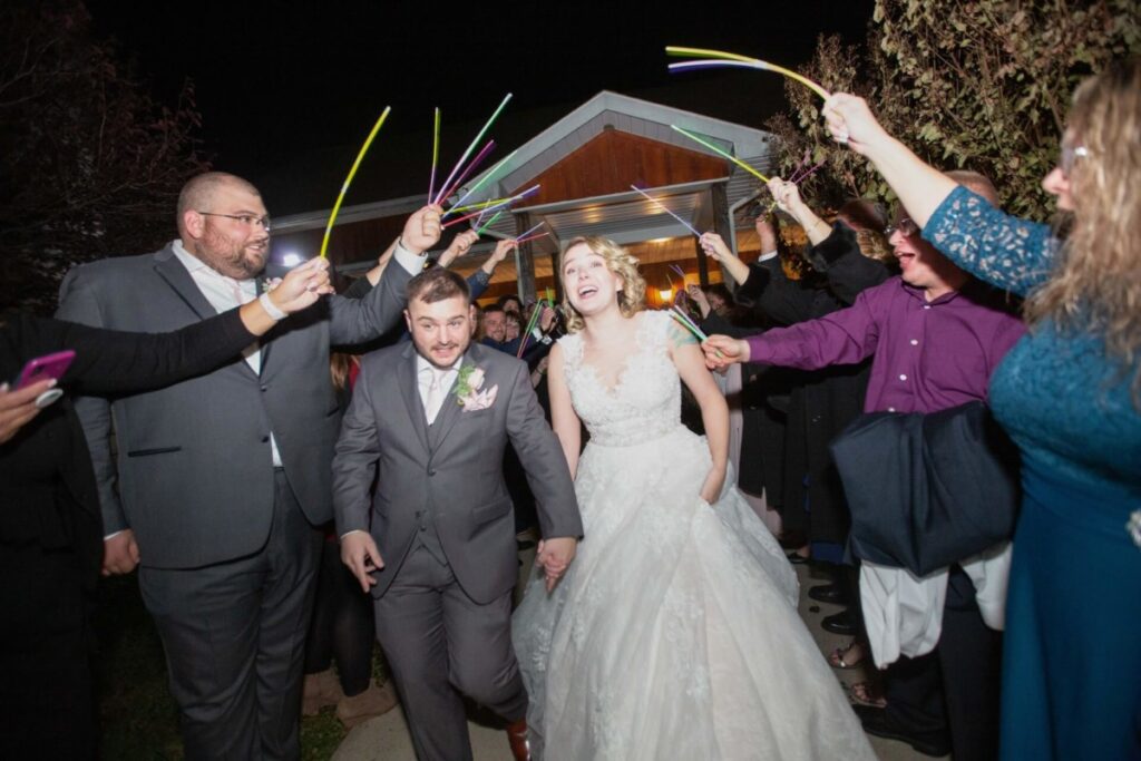 Bride and groom walk through a crowd at night, holding glow sticks.