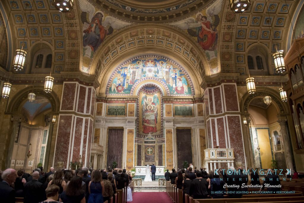 Interior of a large, ornate church with a tall arched ceiling, intricate frescoes, and a congregation seated facing an altar.