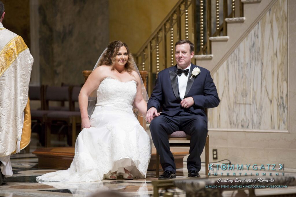 Bride and groom seated during a wedding ceremony in a church, holding hands.