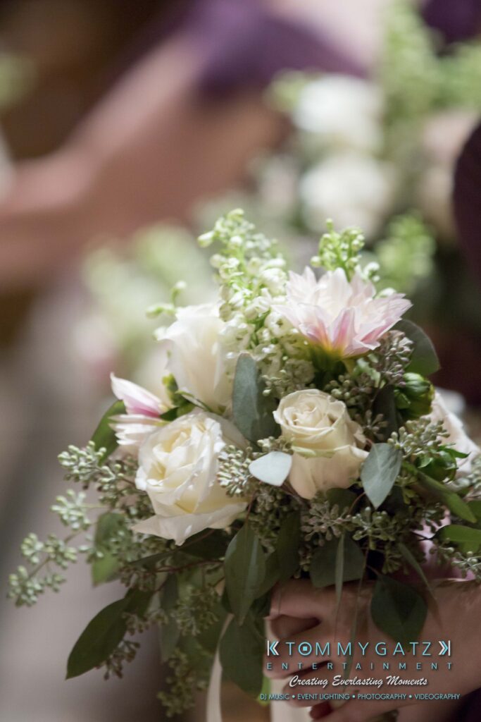 Close-up of a wedding bouquet featuring white roses, small white flowers, and eucalyptus leaves.