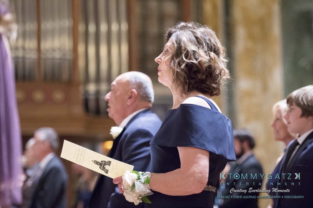 A woman in a blue dress holds a program at a formal event, with other attendees in the background.