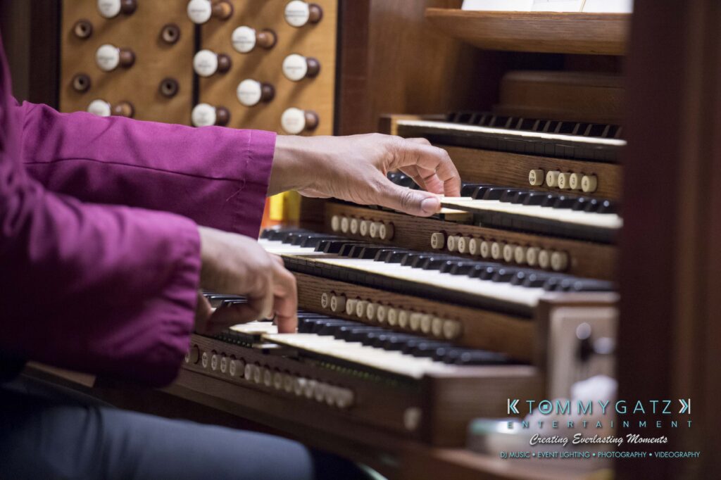 Hands playing an organ with multiple keyboards and buttons, wearing a red sleeve.