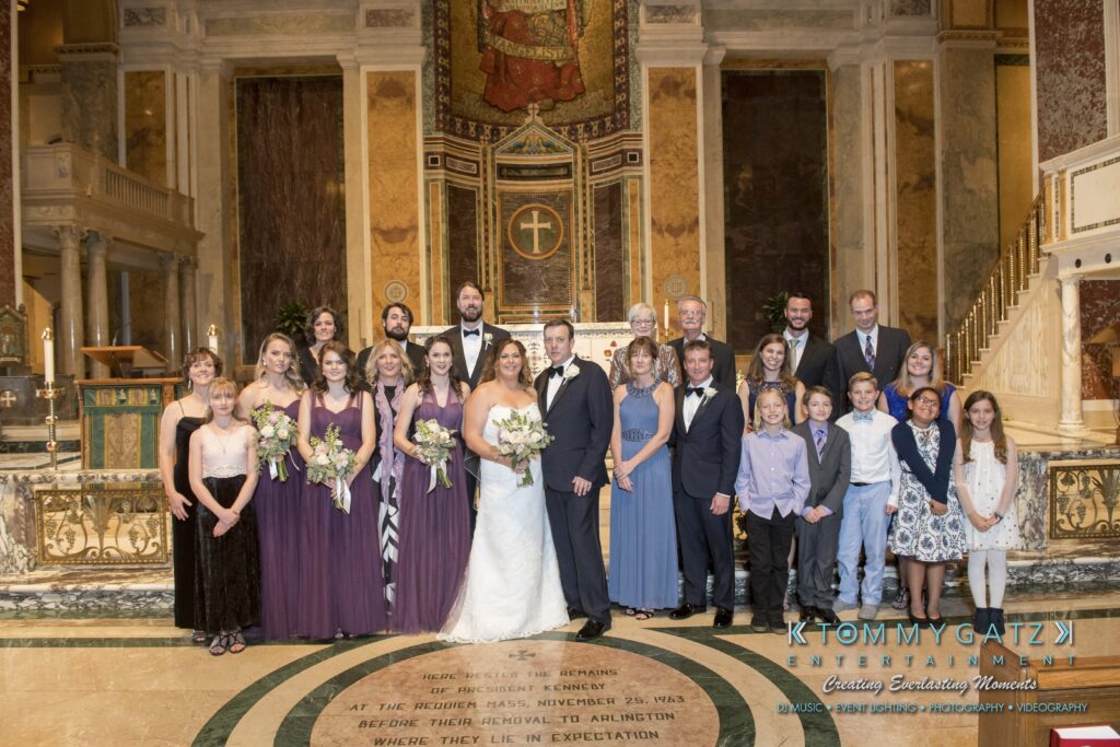 A wedding party with a bride, groom, and guests posing indoors at the altar.