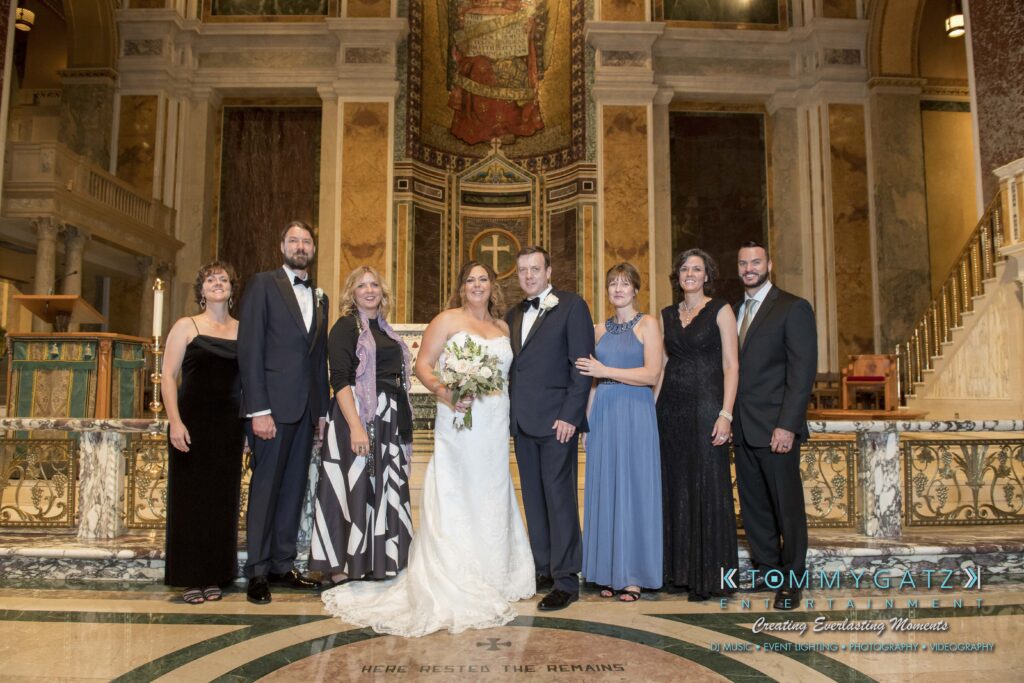 A wedding party poses for a group photo inside a cathedral, featuring the bride, groom, and six attendees in formal attire.
