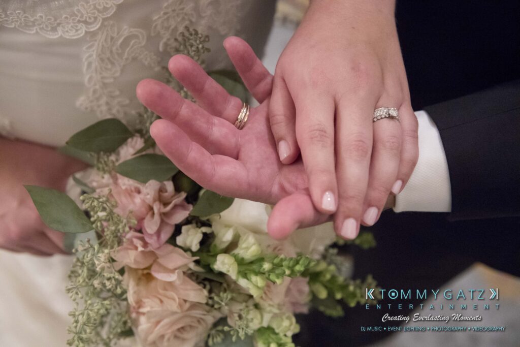 Close-up of a couple's hands with wedding rings, resting on a bouquet of flowers.
