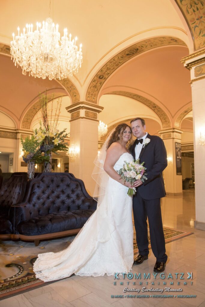Bride and groom posing together in a grand lobby with elegant chandeliers and ornate architecture.