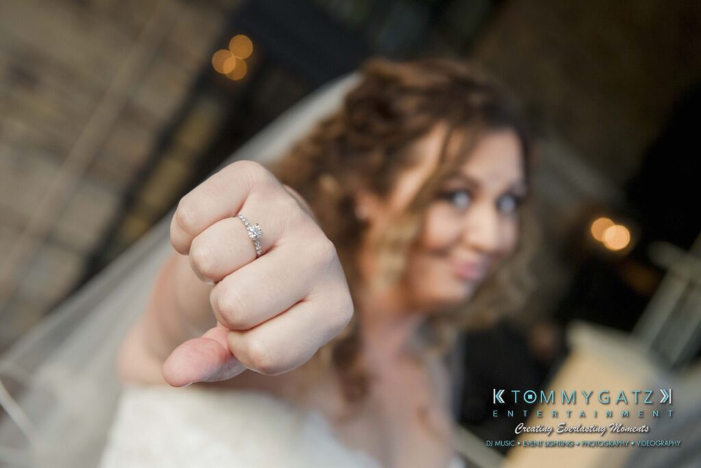 Bride wearing a wedding dress shows her engagement ring, extending her fist towards the camera.