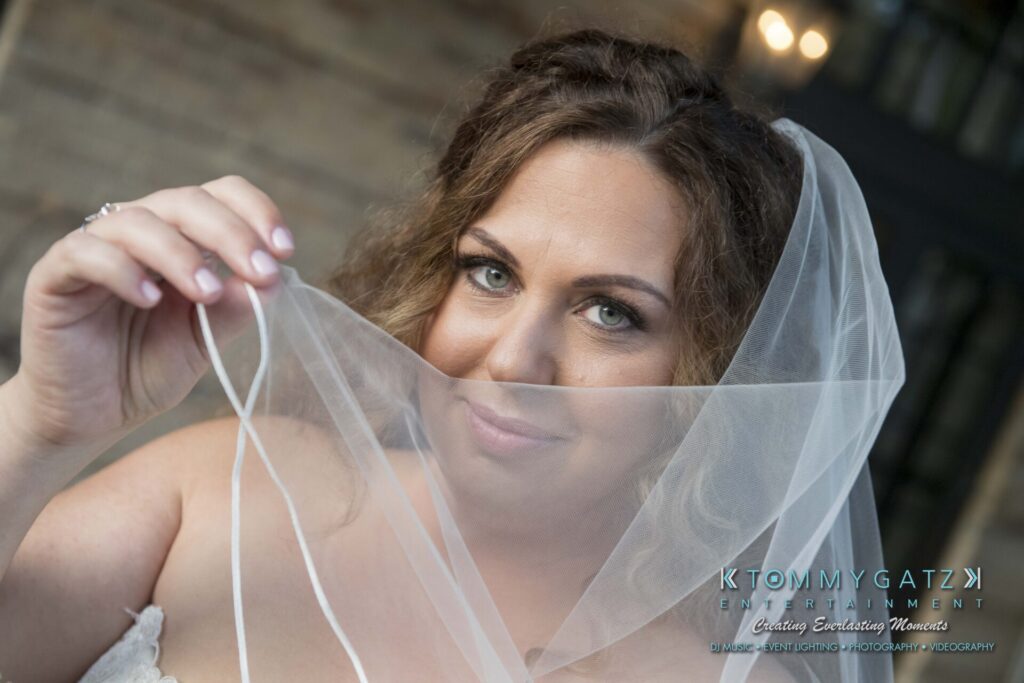 A bride holding her veil over her face, looking directly at the camera with a soft smile.