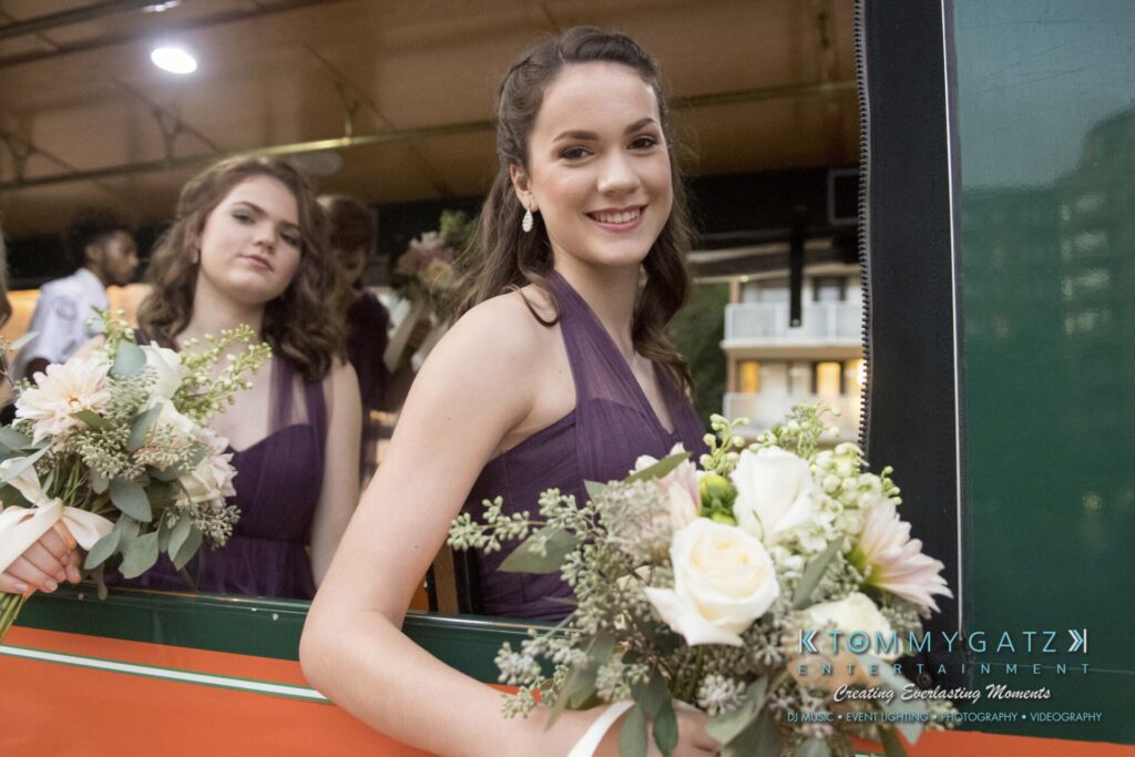 Two women in purple dresses hold flower bouquets inside a vehicle.