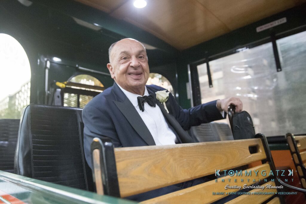 A man in formal attire, wearing a boutonniere, sits inside a trolley car.