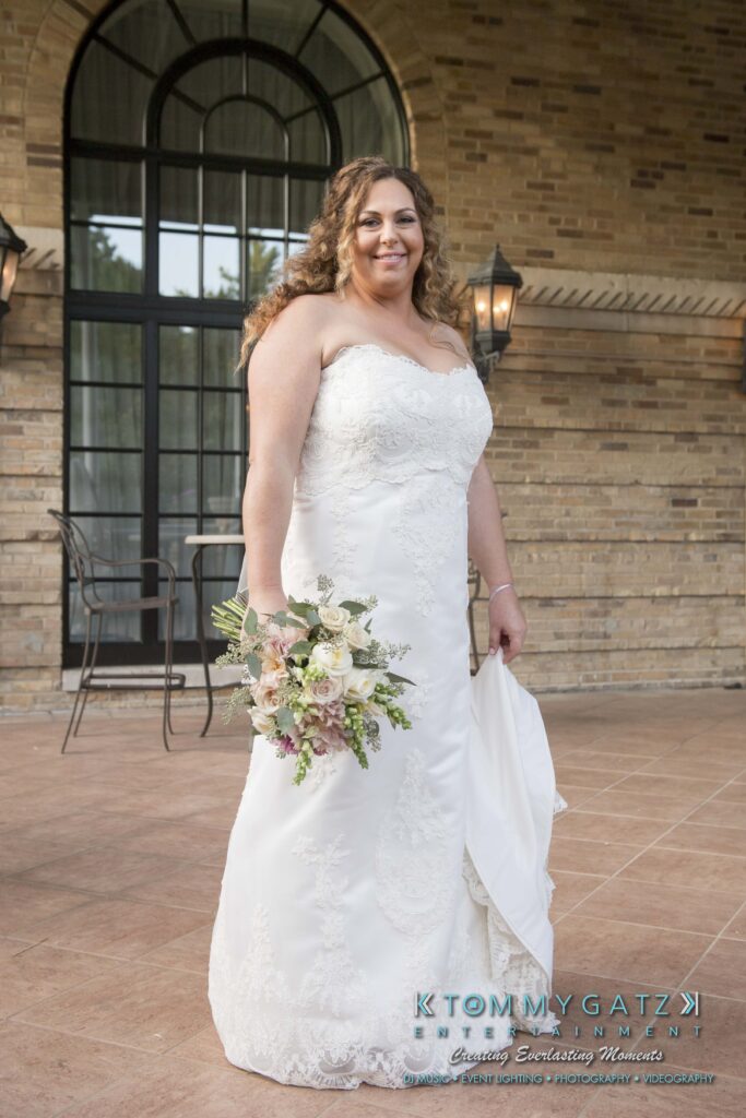 A woman in a white wedding dress holds a bouquet of flowers standing outside a brick building.