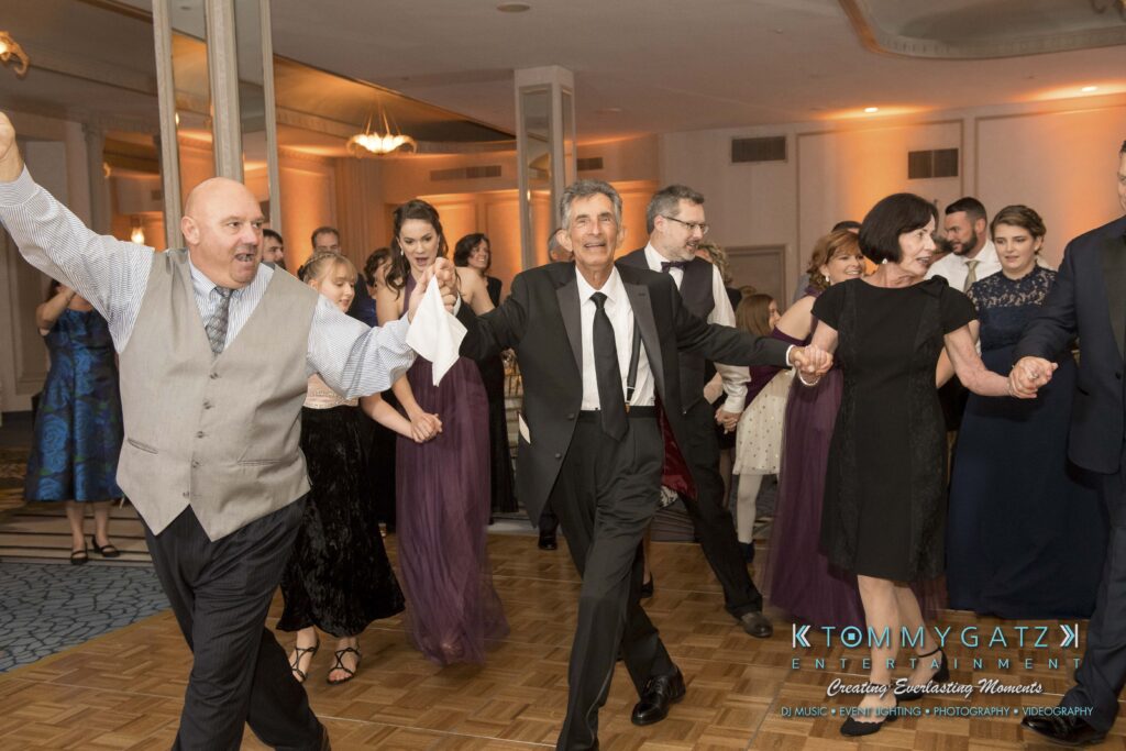 People in formal attire are holding hands and dancing in a ballroom.