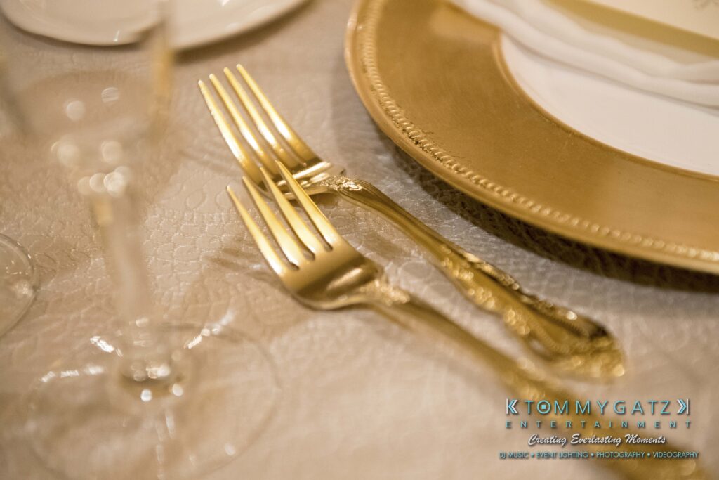 Elegant table setting with golden forks, a decorative plate, and a champagne flute on a patterned tablecloth.